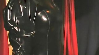 Gorgeous mistress clad in a latex suit teases her buxom slave